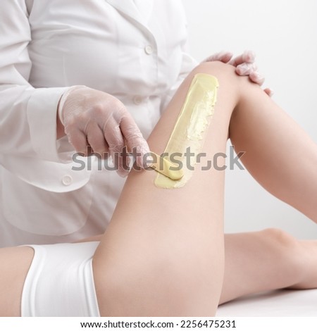 Waxing procedure - applying green hot wax on skin leg using spatula while woman lying down on couch. Depilation process with hot wax in beauty salon. Part of photo series.