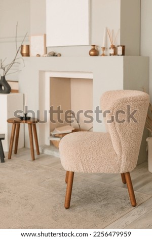 Modern living room interior with chair, wooden table, stack of magazines in decorative fireplace, blank textured canvas on the wall. Modern home decor. Template.