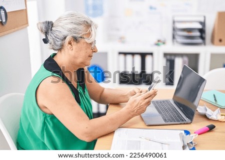 Middle age grey-haired woman business worker using laptop and smartphone at office