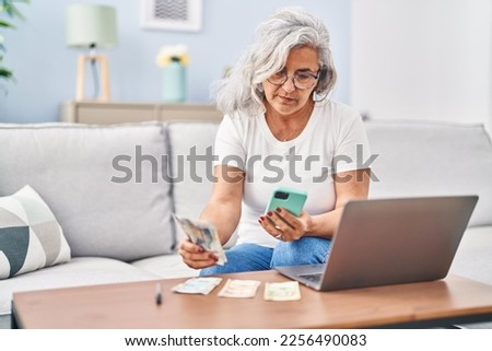 Middle age woman accounting using laptop and smartphone sitting on sofa at home