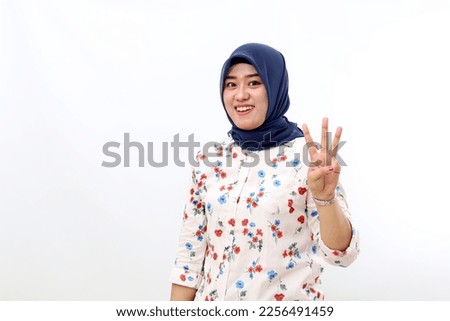 Happy asian muslim woman standing while showing three fingers. Isolated on white background