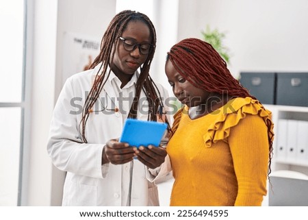 African american women doctor and patient using touchpad having consultation at clinic