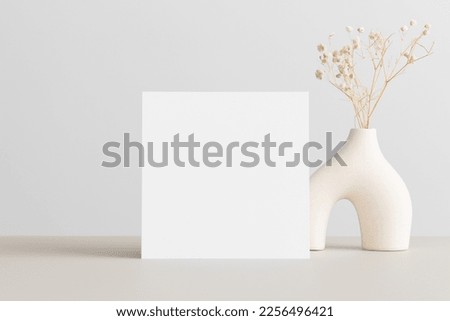 Square invitation card mockup with a gypsophila decoration  on the beige table.