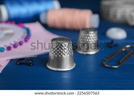 Silver thimble on blue wooden table, space for text. Sewing accessories Royalty-Free Stock Photo #2256507563