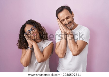 Middle age hispanic couple together over pink background sleeping tired dreaming and posing with hands together while smiling with closed eyes. 