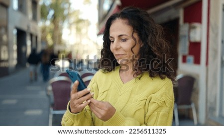 Middle age hispanic woman using smartphone with serious expression at street