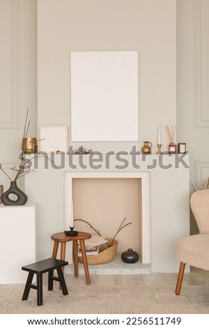 Interior of living room with trendy chair, minimalistic decorative fireplace, modern decor, blank picture frames, wooden stool and table. Mockup, copy space. Minimalistic concept of home decor. 