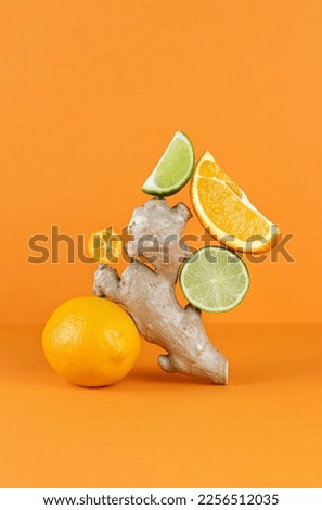 Balancing citrus fruits on the table. Citrus pyramid: lime, orange, ginger and lemon on an orange background. Ingredients for preparing a drink for colds and flu. Copy Space. Royalty-Free Stock Photo #2256512035