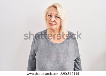 Middle age caucasian woman standing over white background relaxed with serious expression on face. simple and natural looking at the camera.  Royalty-Free Stock Photo #2256512115