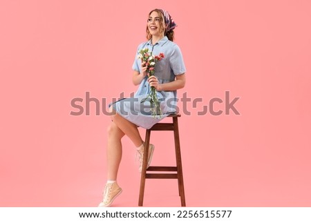 Beautiful happy young woman with bouquet of flowers sitting on stool against pink background