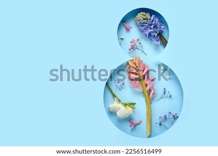 Spring flowers visible through cut color paper in shape of figure 8. Women's Day celebration Royalty-Free Stock Photo #2256516499