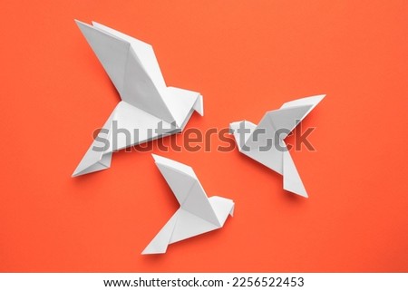 Beautiful white origami birds on orange background, flat lay Royalty-Free Stock Photo #2256522453