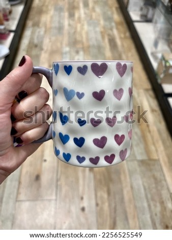 A woman holding a coffee mug that has a gradient of colorful hearts on it. They are pink, purple, and blue.