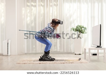 Full length profile shot of a young woman skiing and wearing a virtual reality headset in front of tv at home