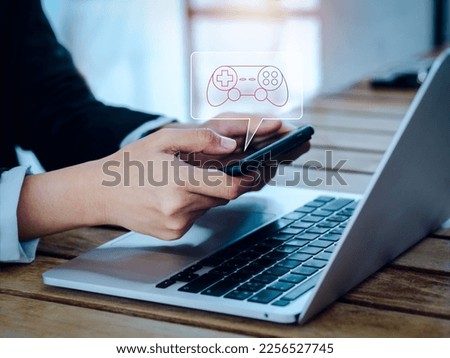 Game controller, joystick icon in bubble speech symbol appear on smart mobile phone in businessperson's hands, horizontal, while working laptop computer. Mobile game, smartphone gaming mode concept.