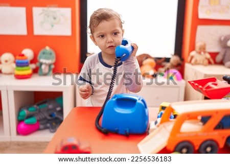 Adorable caucasian boy playing telephone toy standing at kindergarten
