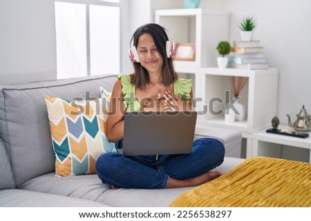 Hispanic young woman using laptop at home smiling with hands on chest with closed eyes and grateful gesture on face. health concept. 