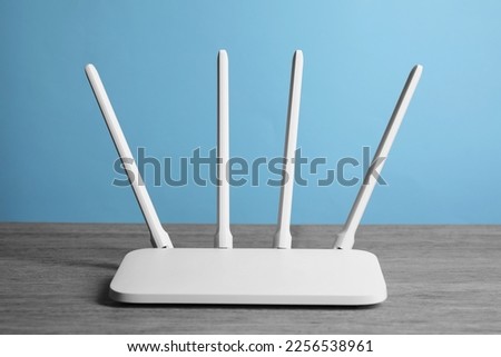 New white Wi-Fi router on wooden table against light blue background Royalty-Free Stock Photo #2256538961