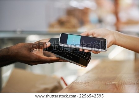 Hand of customer using banking app when paying for purchase in bakery