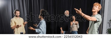 young redhead man posing with outstretched hand near interracial actors talking in acting school, banner Royalty-Free Stock Photo #2256552043