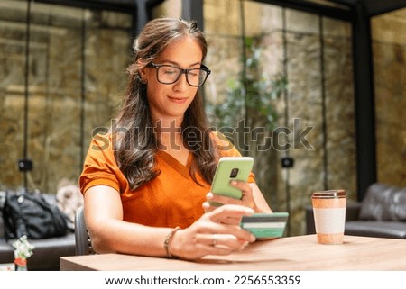 brazilian woman photographing credit card with mobile at table