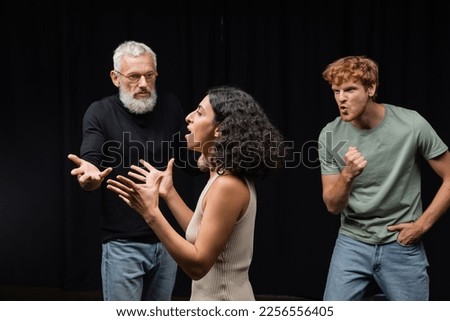 multicultural actress rehearsing near gesturing acting skills teacher and emotional redhead man in theater Royalty-Free Stock Photo #2256556405