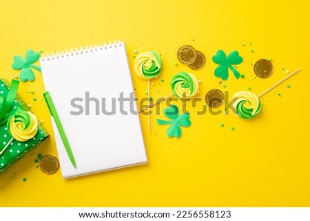 St Patrick's Day concept. Top view photo of notepad pen meringue candies sprinkles gold coins gift box and clovers on isolated vibrant yellow background with empty space