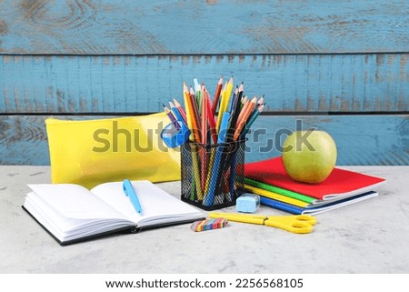 Holder with stationery, open notebook, copybooks, pencil case and apple on wooden background