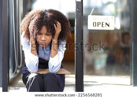 Young African woman running a small start-up business sits at the entrance looking absent-minded.