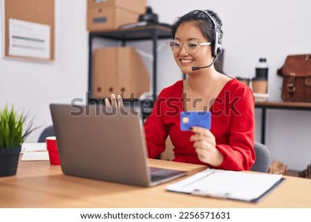 Asian young woman working using computer laptop and credit card looking positive and happy standing and smiling with a confident smile showing teeth 