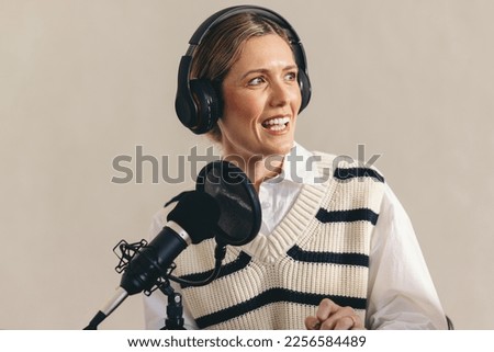 Woman interviewing a guest on her radio show while sitting behind a microphone with a headset. Female radio host recording a live audio broadcast in a studio.