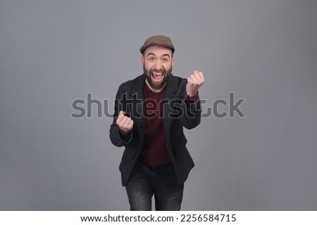 Stylish young man in jacket and cap enthusiastic with arms up in a studio shot