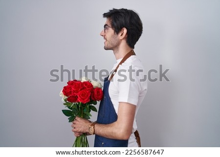 Young hispanic man holding bouquet of white and red roses looking to side, relax profile pose with natural face and confident smile. 