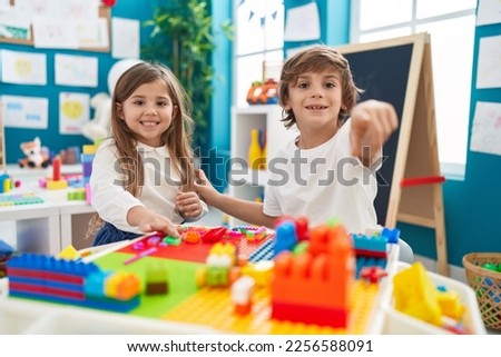 Brother and sister playing with construction blocks sitting on table at kindergarten