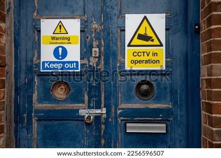 Old large blue wooden door with yellow security and warning signs and old rusty locks 