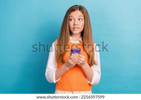 Photo of minded pensive girl biting lips hold telephone look empty space isolated on blue color background