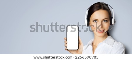 Customer support phone operator in headset holding showing smartphone cell phone mobile white blank mock up screen, isolated over grey background. Consulting and assistance service call center. zoom