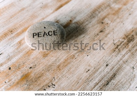 A grey stone with the inscription peace lying on a wooden table. High quality photo