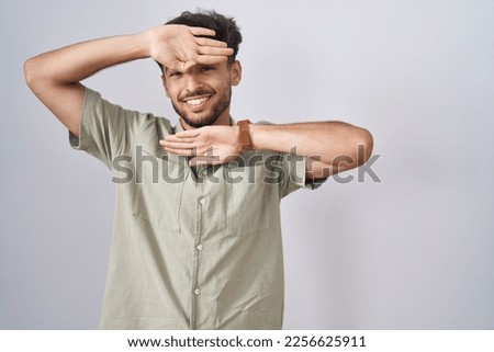 Arab man with beard standing over white background smiling cheerful playing peek a boo with hands showing face. surprised and exited 