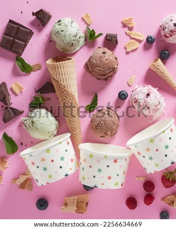Overhead composition of colorful ice cream scoops with waffle cones and chocolate near bowls and berries placed on pink background