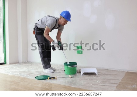 Builder in the room mixes paint in a bucket, apartment renovation. Preparing to paint the wall in the house Royalty-Free Stock Photo #2256637247