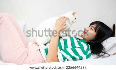 Portrait of young Asian woman holding cute White cat laying on sofa. Female hugging her cute short hair kitty in her home. Adorable domestic pet concept.