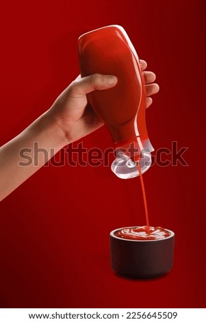 Tomato ketchup concept, a male hand squeezing ketchup bottle and the ketchup pouring in a bowl Royalty-Free Stock Photo #2256645509