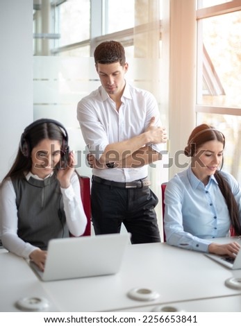 Handsome male mentor teaching, supervising and giving instructions to call centar workers in office Royalty-Free Stock Photo #2256653841