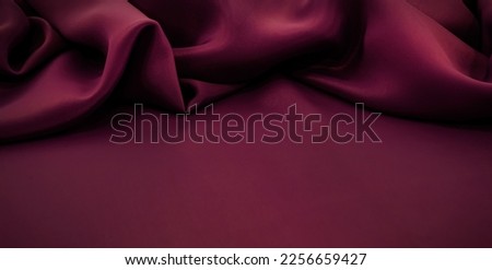 Texture of a smooth luxurious, elegant fabric in burgundy, purple, red. Purple satin or silk fabric with folds and waves