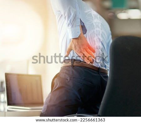 Businessman, back pain and x ray of spine from sitting and working by laptop on desk chair at the office. Employee male suffering spinal injury or slip disk with ache, inflammation or painful join