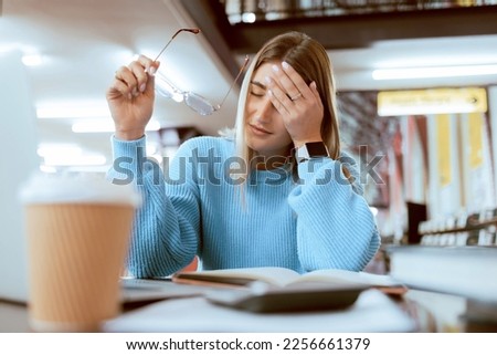 Woman student, tired with headache and university burnout, stress about paper deadline or study for exam in library. Campus, college studying fatigue with scholarship problem, pain and mental health Royalty-Free Stock Photo #2256661379