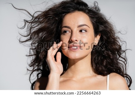 Young brunette woman touching freckled skin isolated on grey Royalty-Free Stock Photo #2256664263