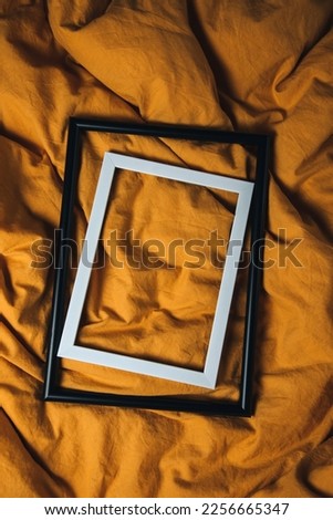 Background for design. White and black frames on yellow rumpled fabric. Flat lay, copy space