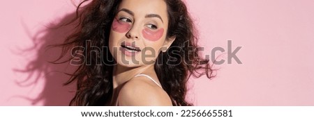Positive young woman with hydrogel eye patches standing on pink background, banner